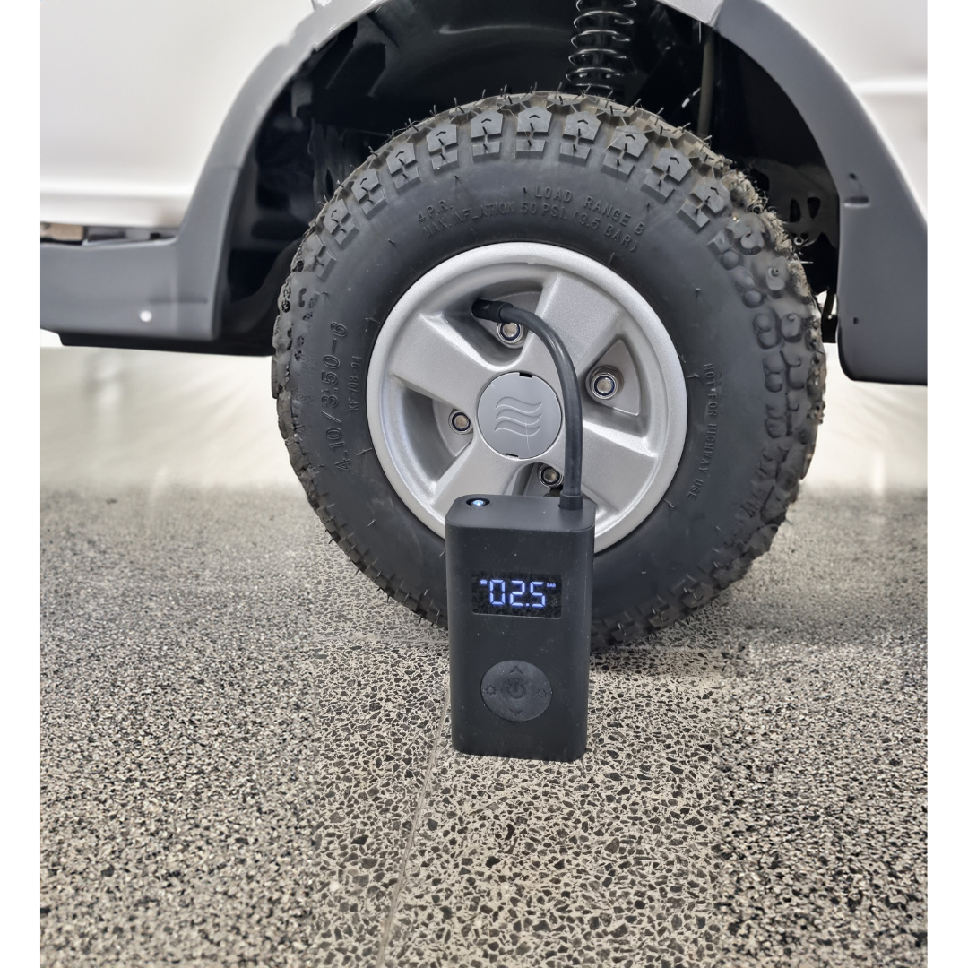 A close-up of a customized car tire on a textured surface showcases precision. In front, an Afikim Electric Vehicle Accessories portable air compressor shows 0.25 on its digital display, indicating tire pressure and highlighting customization options for enthusiasts.